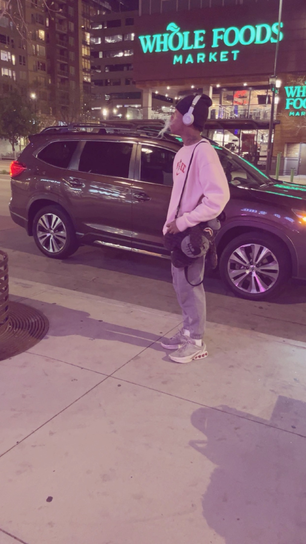 A young artist exhales into the night air on a downtown Denver corner, headphones on, streetlight glowing violet behind him.
